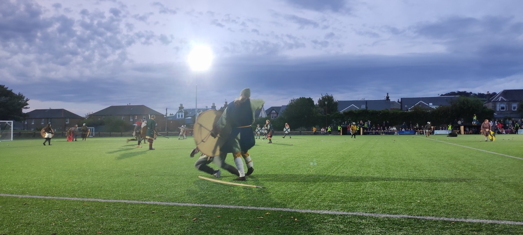 Viking reenactors clashing with shields and spears during the evening battle reenactment, floodlights overhead
